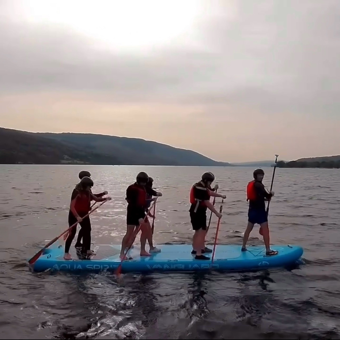 a giant paddle board on a lake with 5 people on